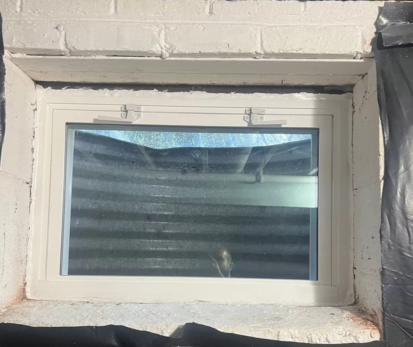 Basement window installation with visible insulation and plastic sheeting