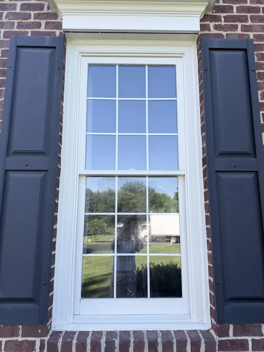 Exterior view of a residential window with shutters and brick facade
