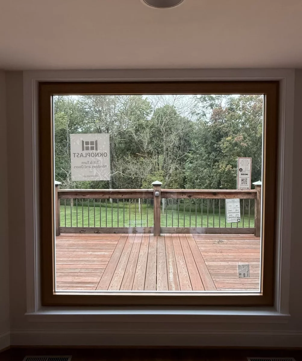 Large window with wood trim overlooking a deck and backyard