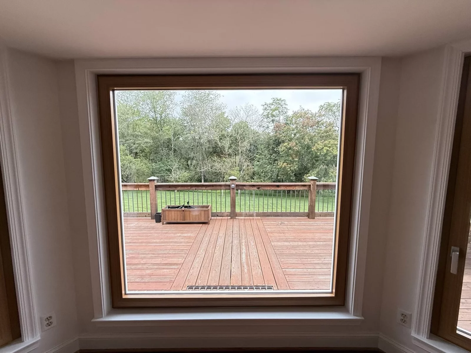Large window with wood trim overlooking a deck and backyard