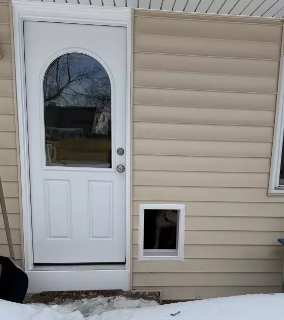 Exterior view of house with white door, window, and installed pet door in snow