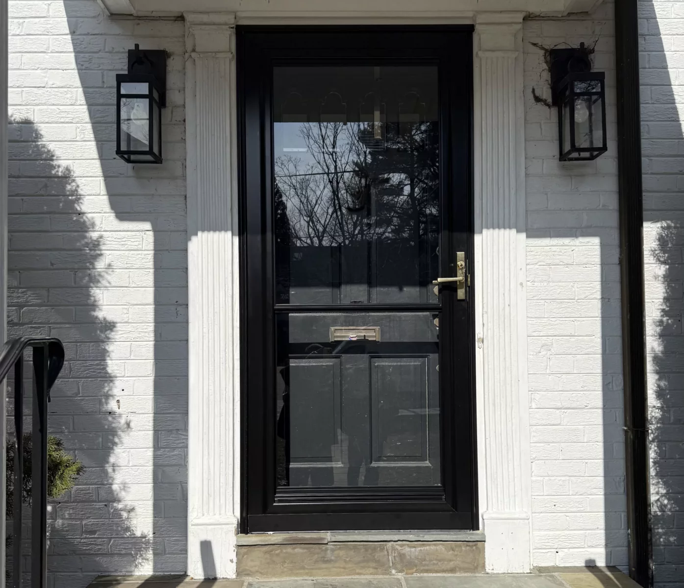 Exterior view of a house with a black storm door and white brick facade