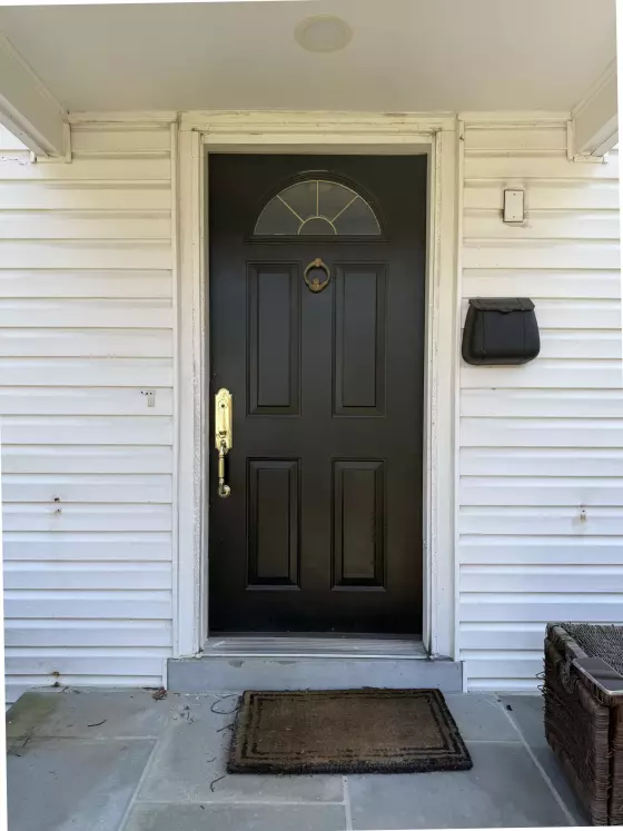 Black exterior door with brass handle and white siding