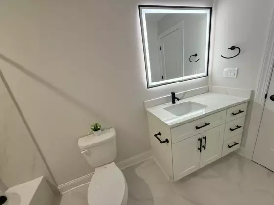 Bathroom vanity with white cabinetry, quartz top, black faucet, and a backlit LED mirror