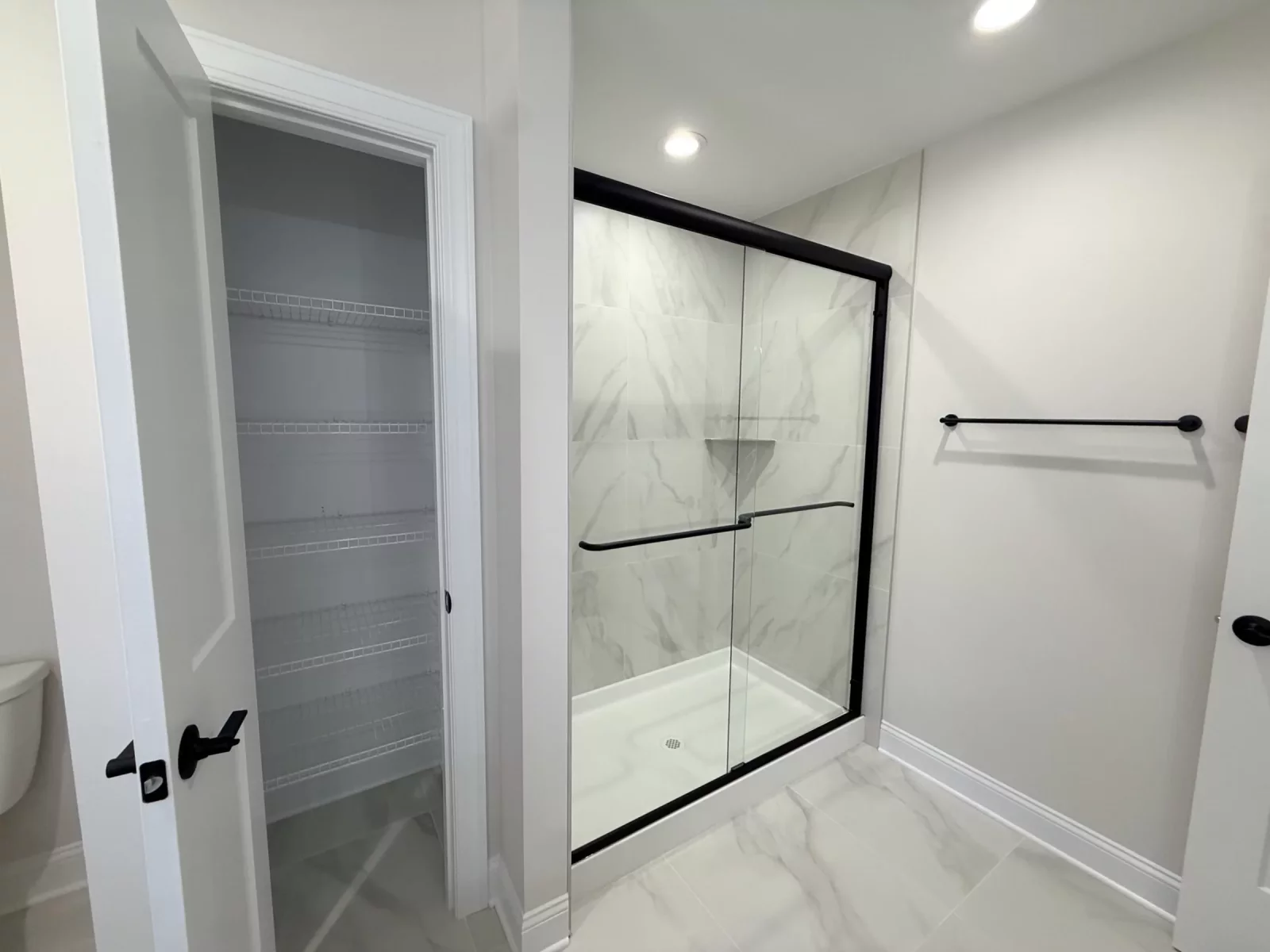 Walk-in shower with marble-look tile and a black-framed glass door next to a wire-shelved closet