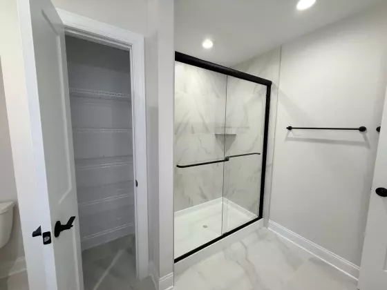Walk-in shower with marble-look tile and a black-framed glass door next to a wire-shelved closet