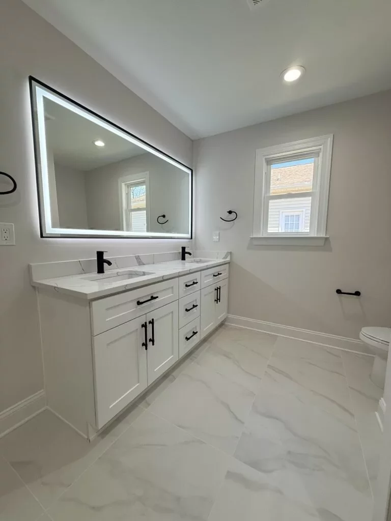 Bathroom with a white double vanity, quartz countertop, backlit LED mirror, and marble-look tile floor