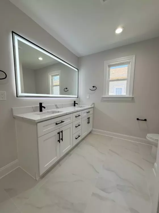Bathroom with a white double vanity, quartz countertop, backlit LED mirror, and marble-look tile floor