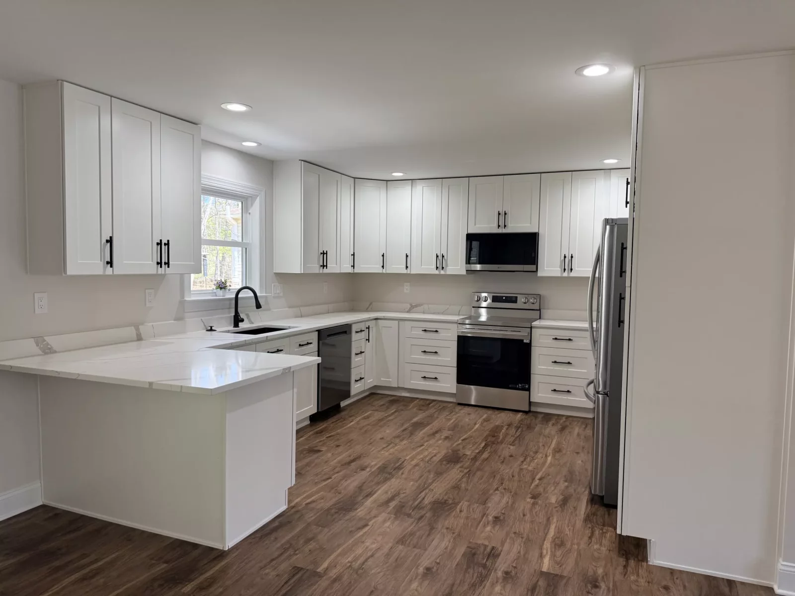 Custom kitchen with white shaker cabinets, marble-look quartz counters, peninsula seating, and stainless steel appliances
