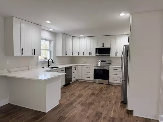 Custom kitchen with white shaker cabinets, marble-look quartz counters, peninsula seating, and stainless steel appliances