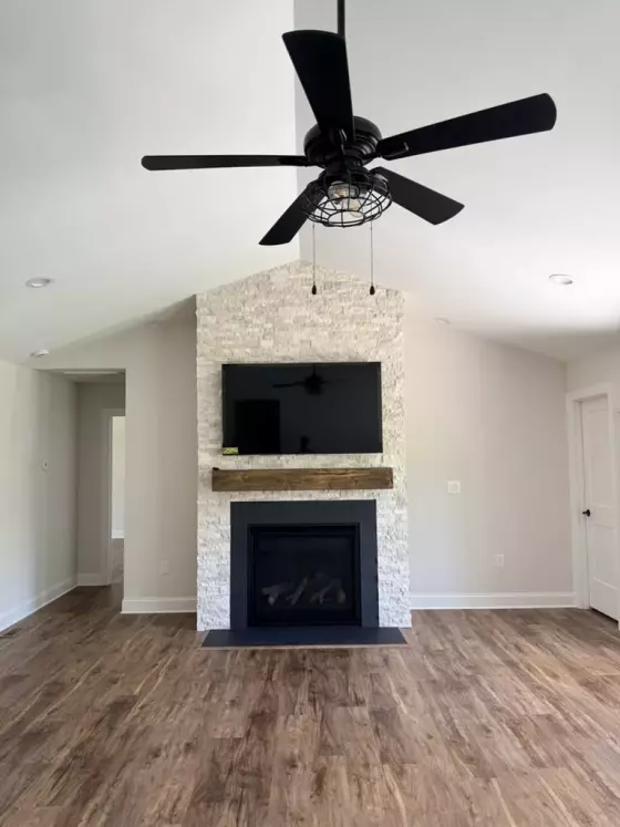 Vaulted living room with a floor-to-ceiling stacked-stone fireplace, mounted TV, and black ceiling fan