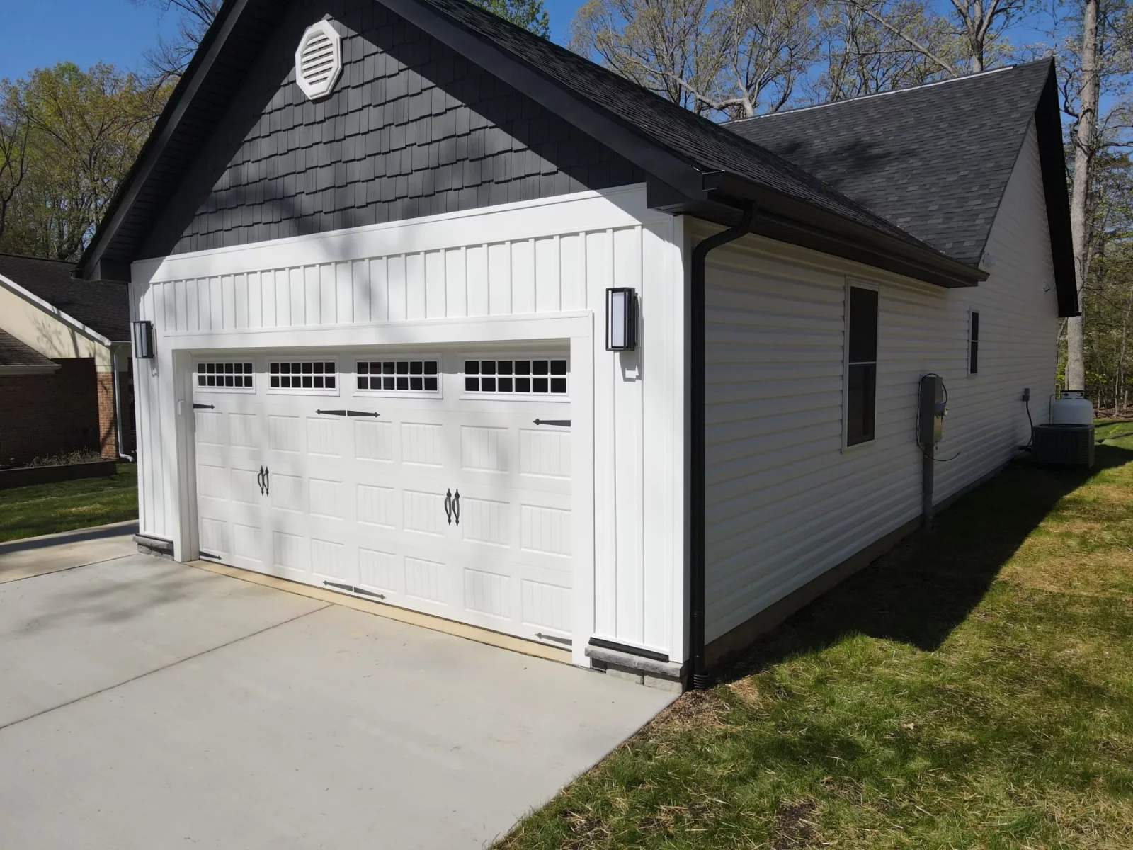 Attached two-car garage with white siding, dark roof, and a paved driveway on a new custom home