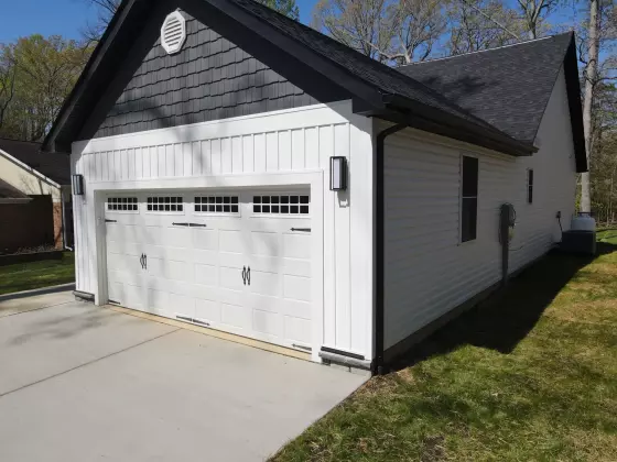Attached two-car garage with white siding, dark roof, and a paved driveway on a new custom home