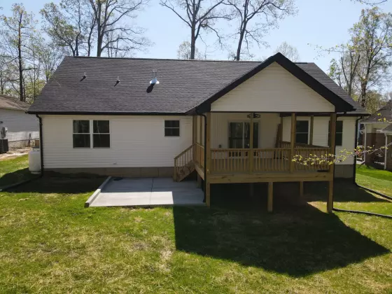 Back exterior of a new custom home with white siding, a raised wood deck, and a spacious grassy backyard