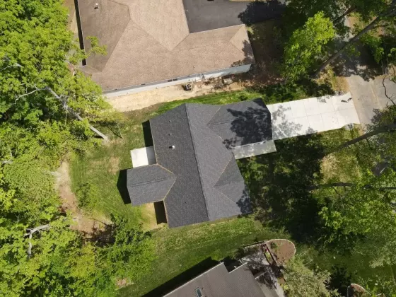 Aerial view of a custom-built home and wooded property with a dark shingle roof and concrete driveway