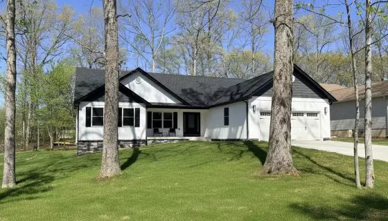 New construction custom home set among mature trees with white siding and a two-car garage
