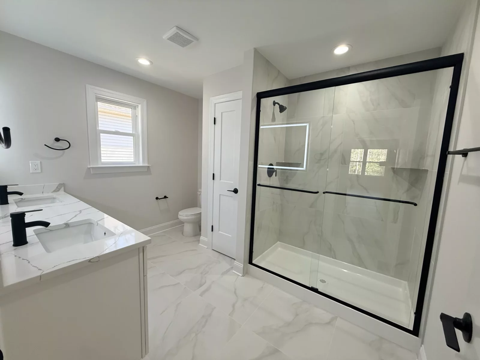 Primary bathroom with a glass walk-in shower, marble-look tile, white vanity, and black fixtures