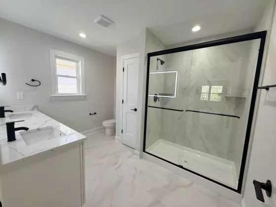 Primary bathroom with a glass walk-in shower, marble-look tile, white vanity, and black fixtures