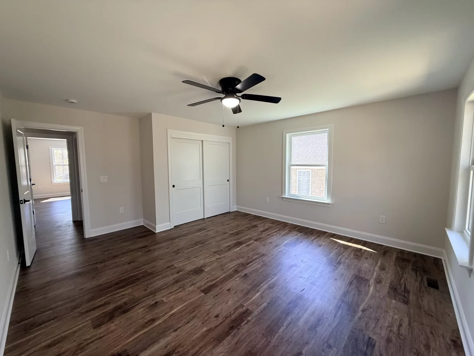 Bright bedroom with a ceiling fan, large window, and wood-look flooring in a newly built home