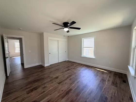 Bright bedroom with a ceiling fan, large window, and wood-look flooring in a newly built home