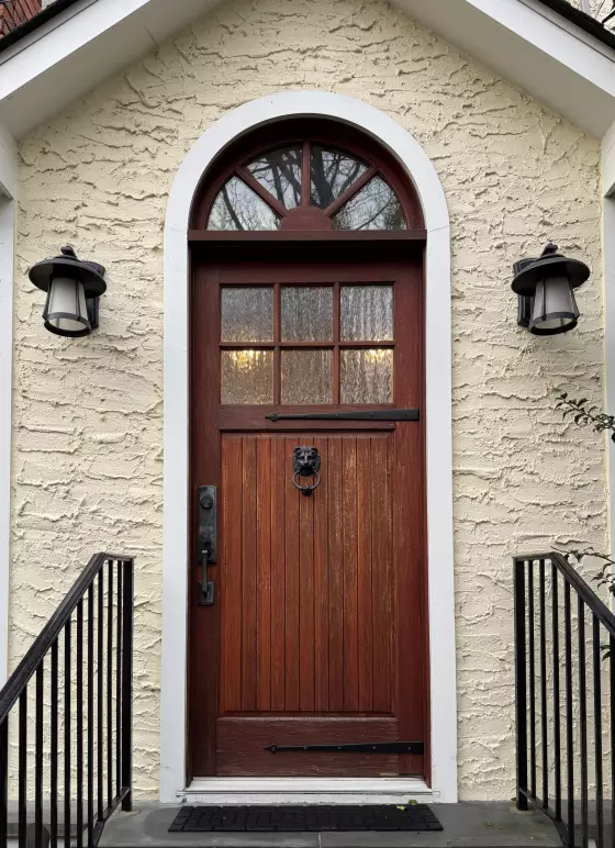 Front view of a wooden entry door with glass panels and stucco facade