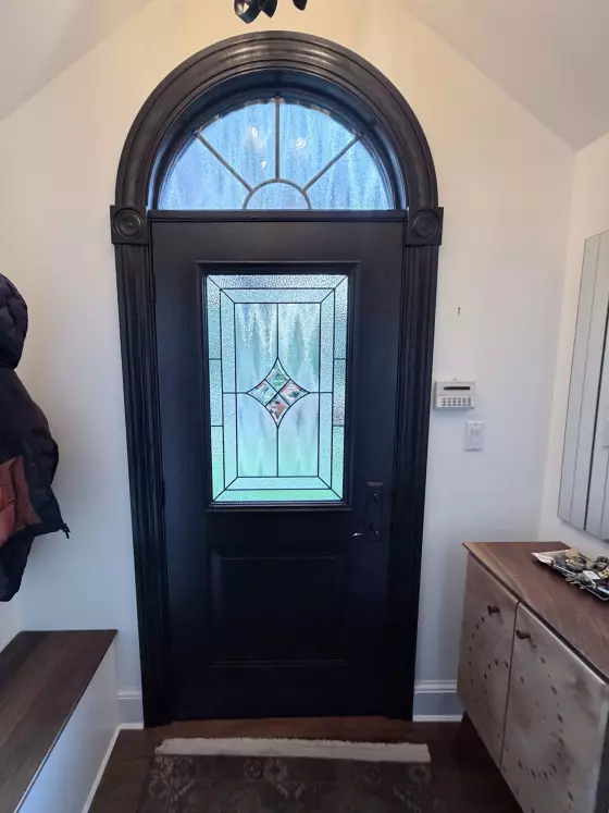 Black entry door with decorative glass panel and arched window inside home