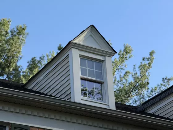 Exterior view of a dormer window with white trim and siding