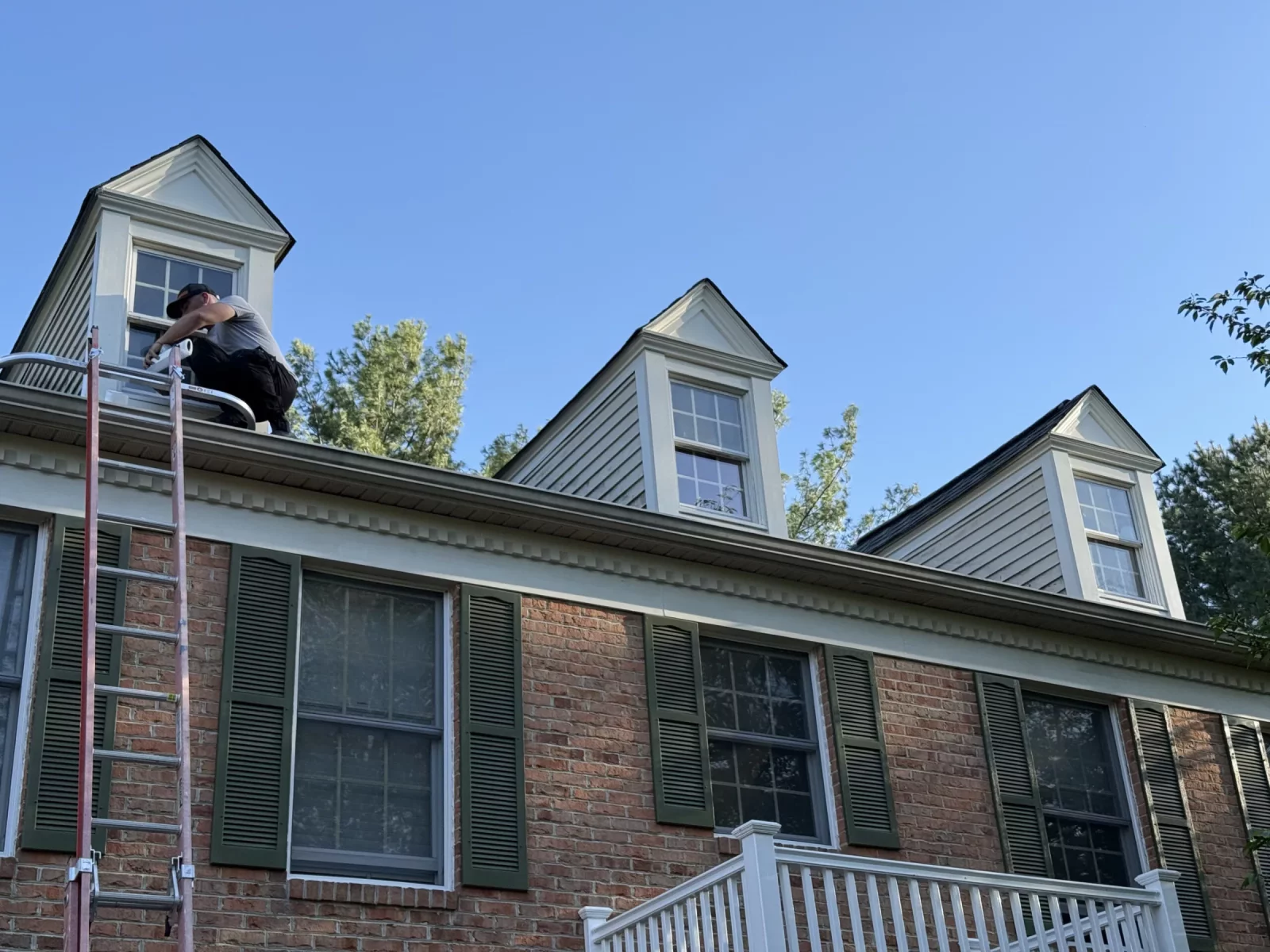 Person on ladder working near windows on house roof exterior