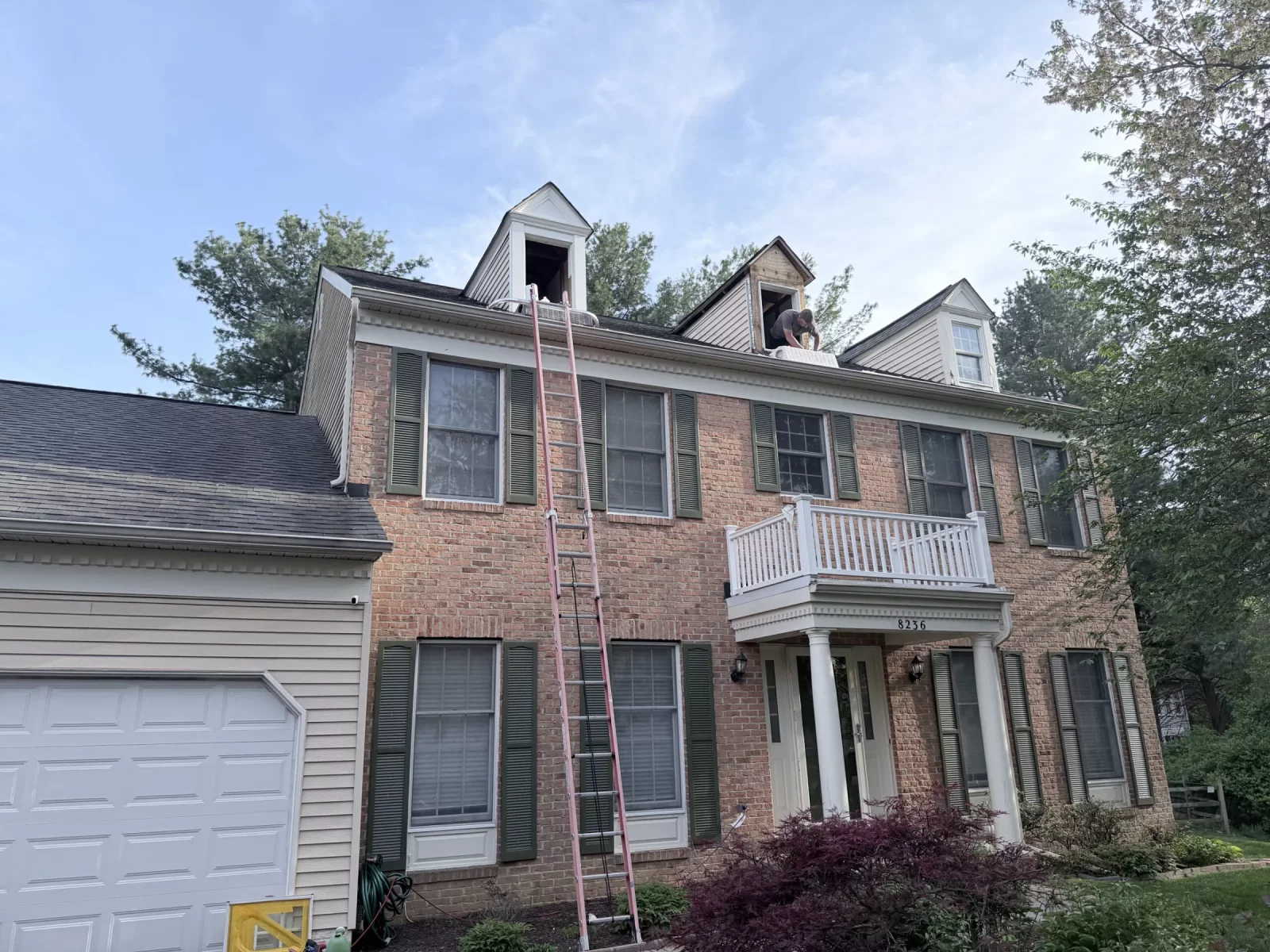 Residential brick house exterior with ladders and workers on roof dormers