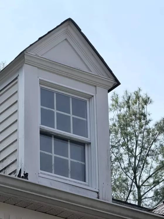 Exterior window with visible rot and damaged trim on residential dormer.