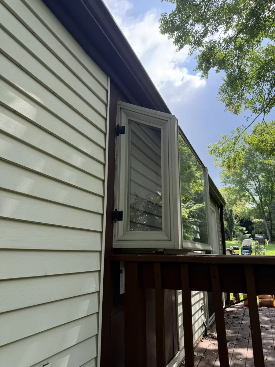 Exterior view of a casement window open on a house with siding and deck railing