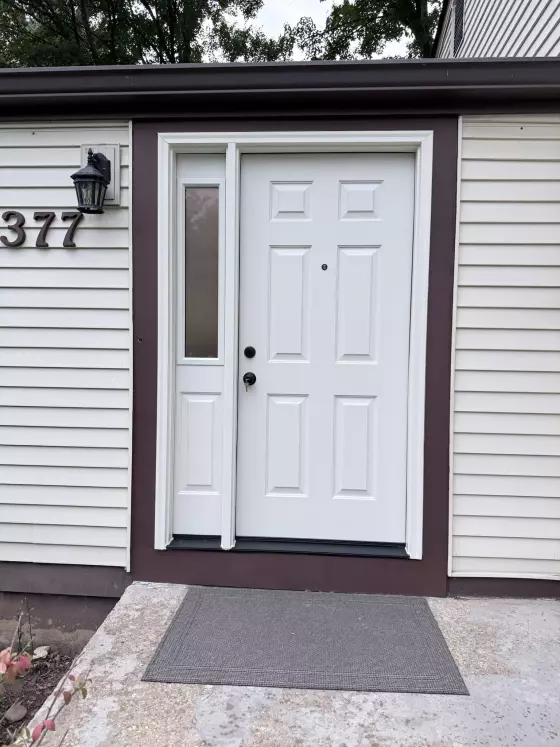 White entry door with side window and brown trim on a house exterior