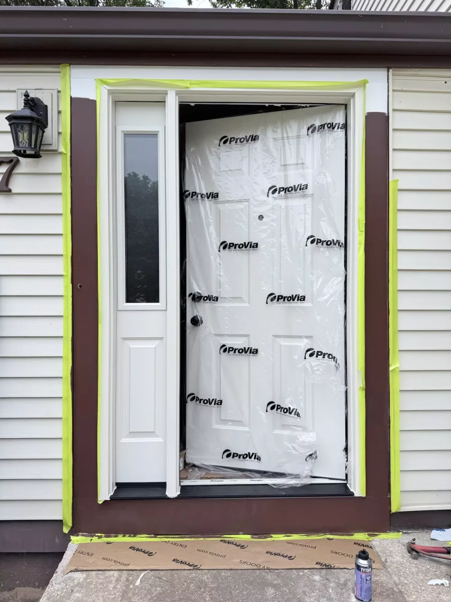 Exterior view of a new entry door being installed with protective film and tools visible