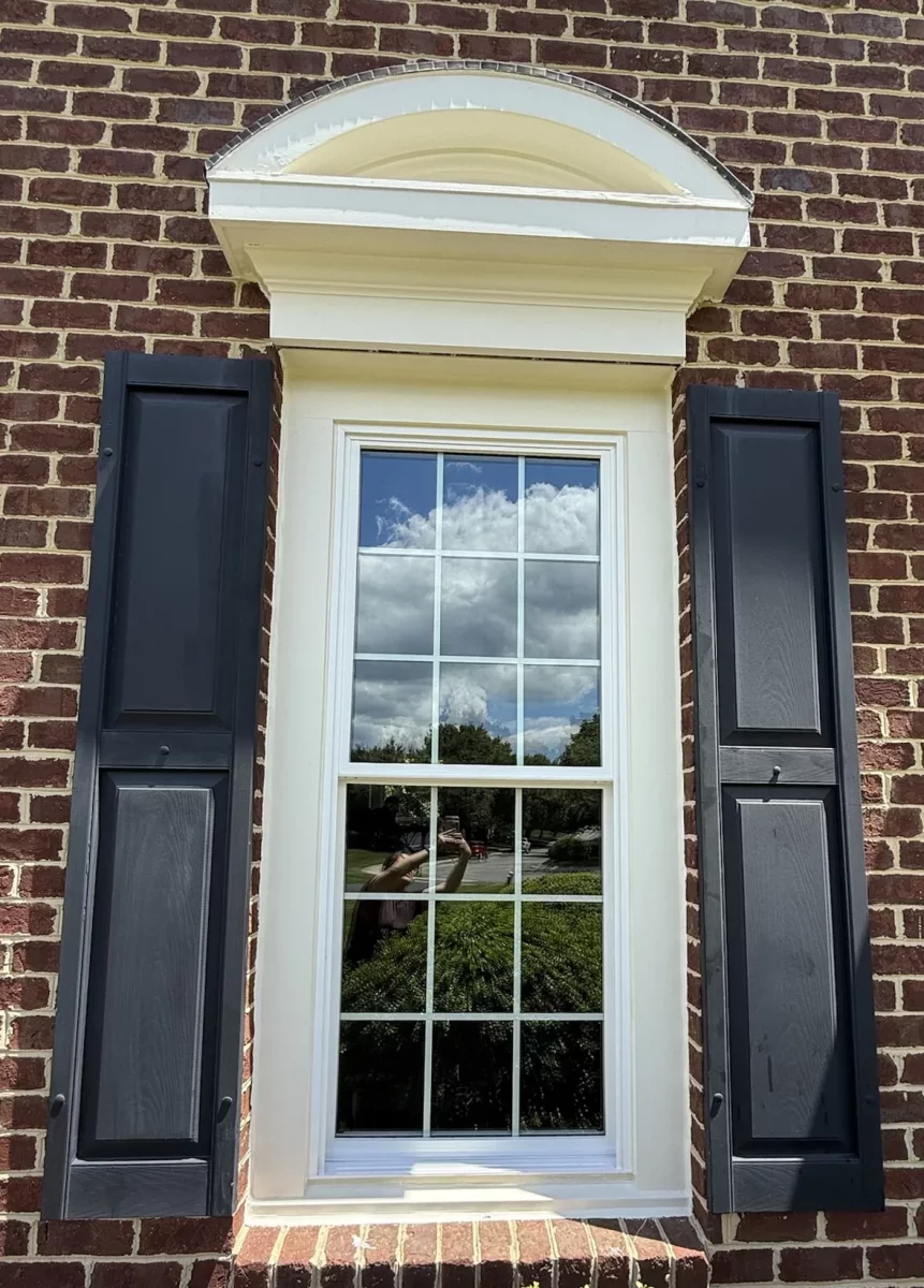 Exterior view of a window with black shutters on a brick wall
