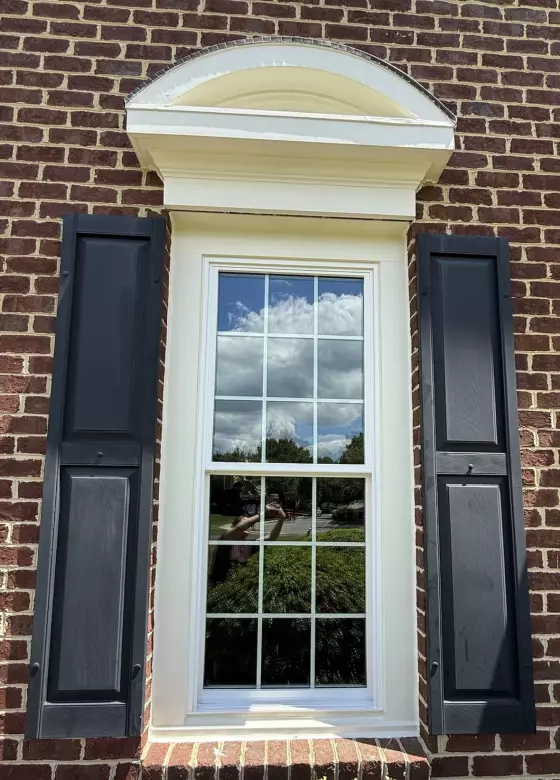 Exterior view of a window with black shutters on a brick wall