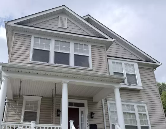 Residential house exterior with beige siding, white trim, and multiple windows