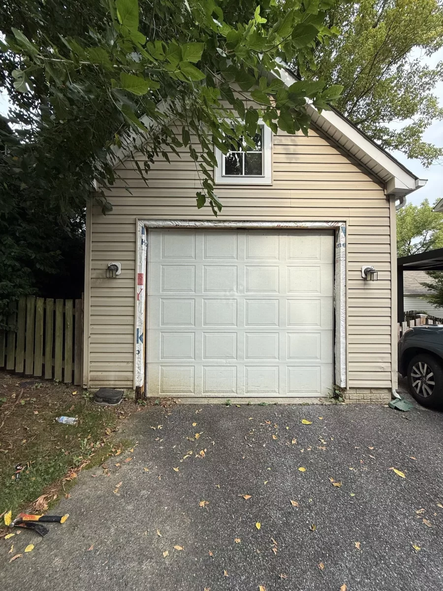 Garage door with exposed trim and tools on driveway