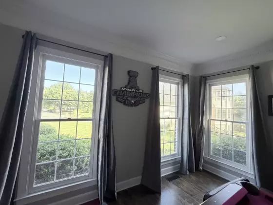 Three large residential windows with white trim and gray curtains in a corner room