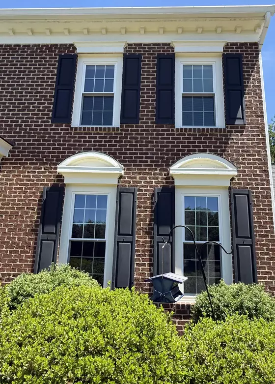 Four double-hung windows with black shutters on a brick house facade