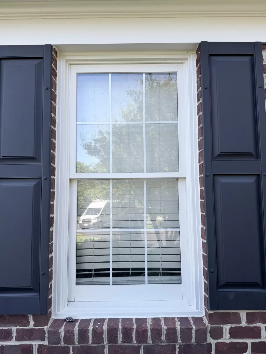 Exterior view of a residential window with shutters and brick facade