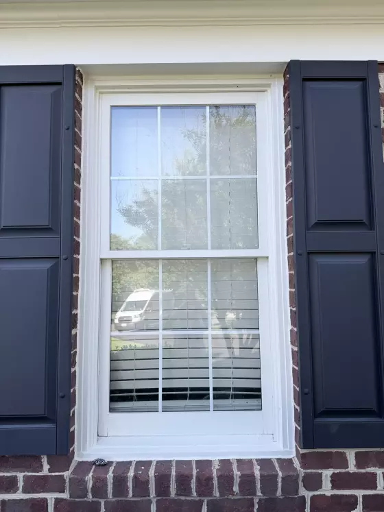 Exterior view of a residential window with shutters and brick facade
