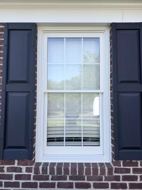 Exterior view of a residential window with brick and shutters