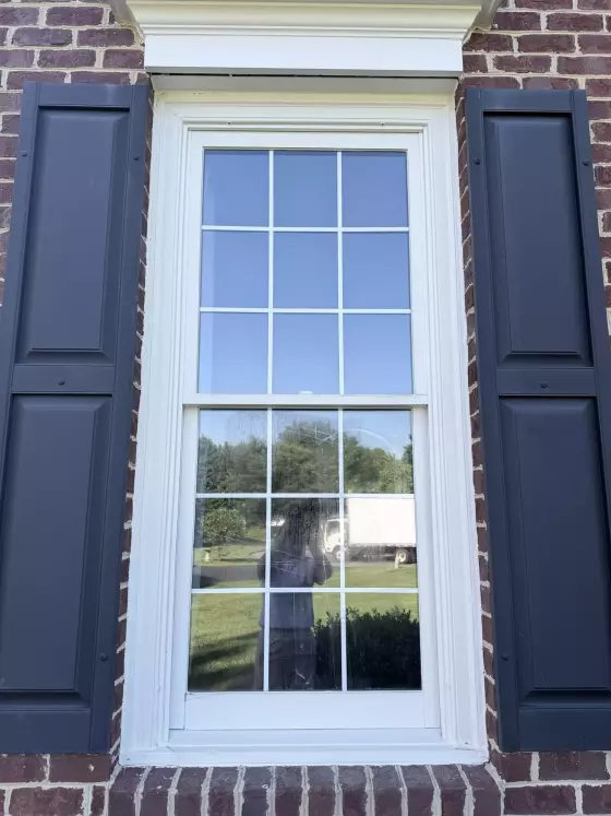 Exterior view of a residential window with shutters and brick facade