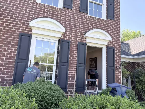 Two workers replacing windows on a brick house exterior
