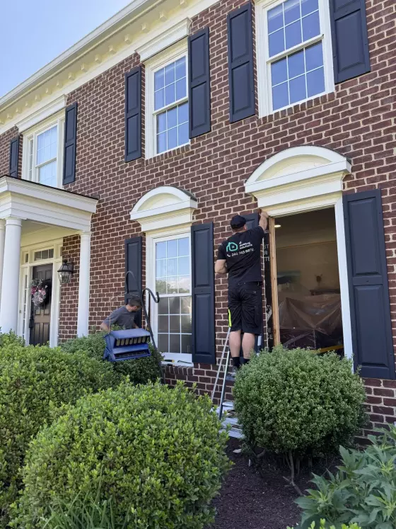 Two workers replacing a window on a brick house exterior