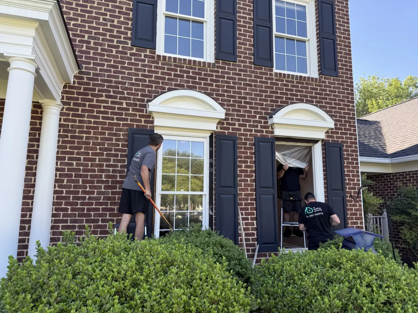 Workers replacing a window on a brick house exterior