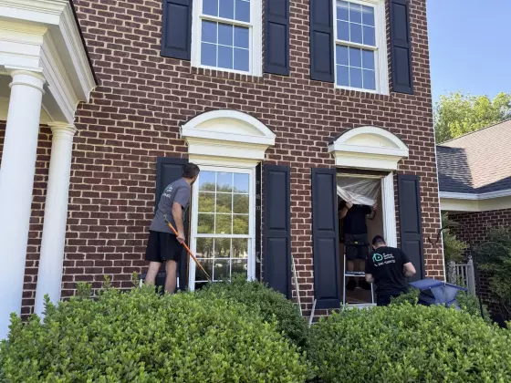 Workers replacing a window on a brick house exterior