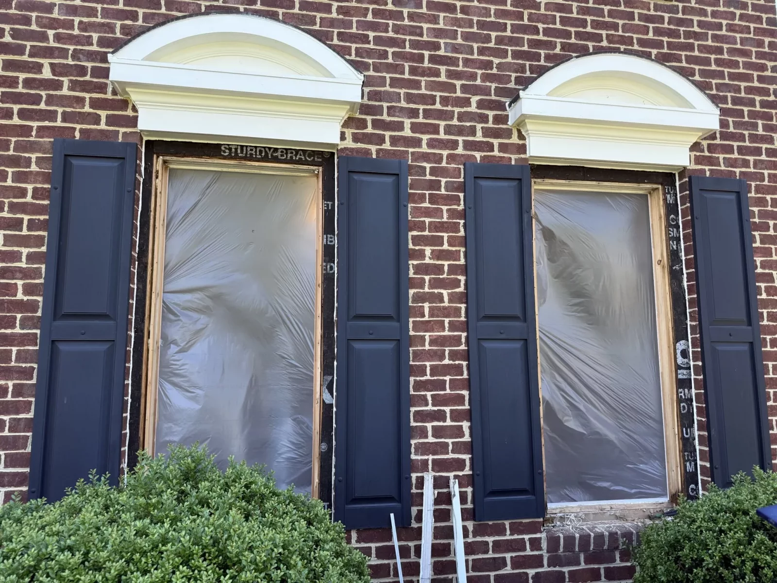 Two window openings with protective film on brick house exterior