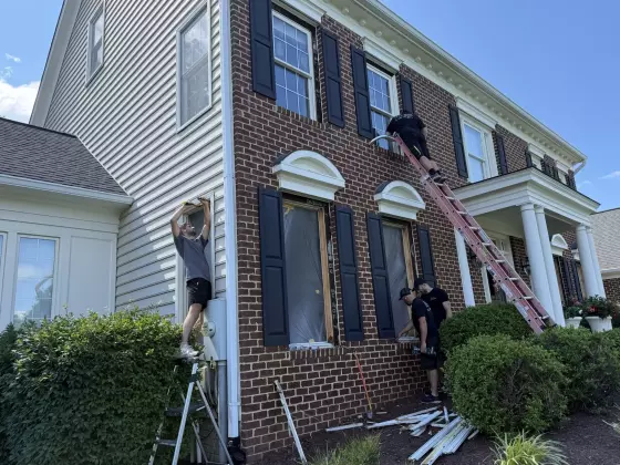 Workers replacing windows on exterior brick house using ladders