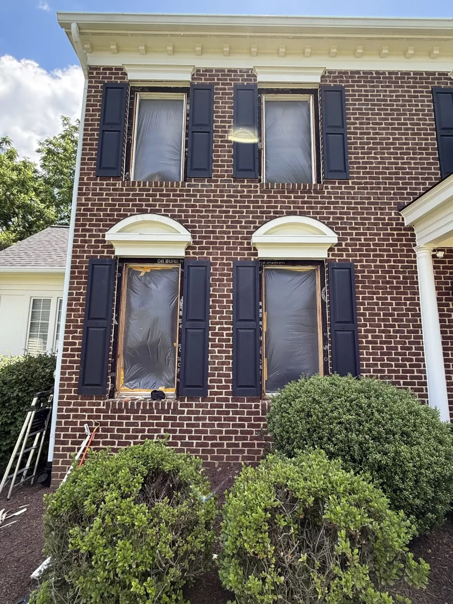 Brick house facade with windows covered in protective film during replacement